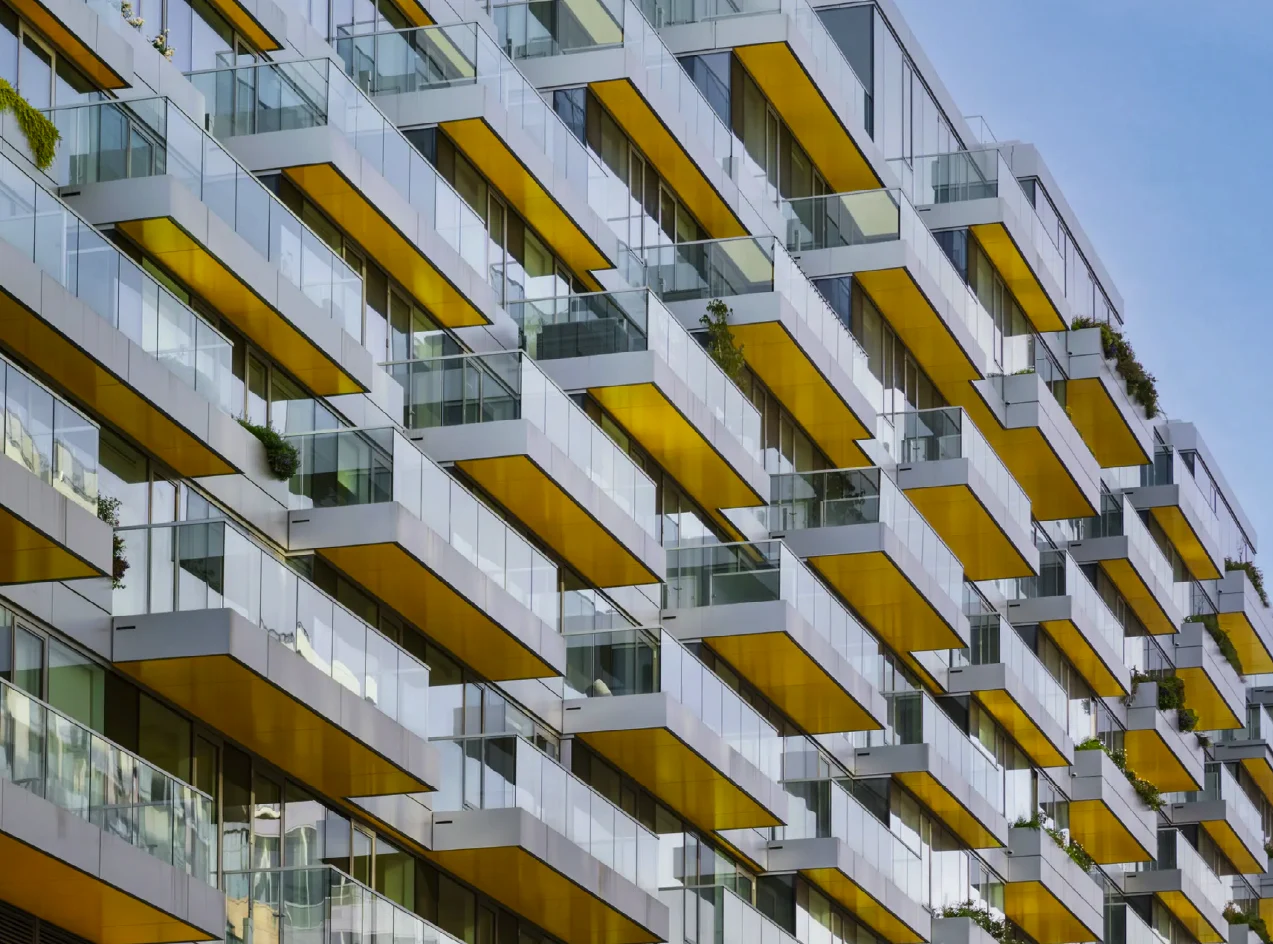 Close photograph of the facade: white balconies, yellow undersides, glass rails and planted terraces