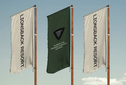 Three flags on timber poles against a blue sky: two cream flags reading Lionsback Resort, a green one with the badge