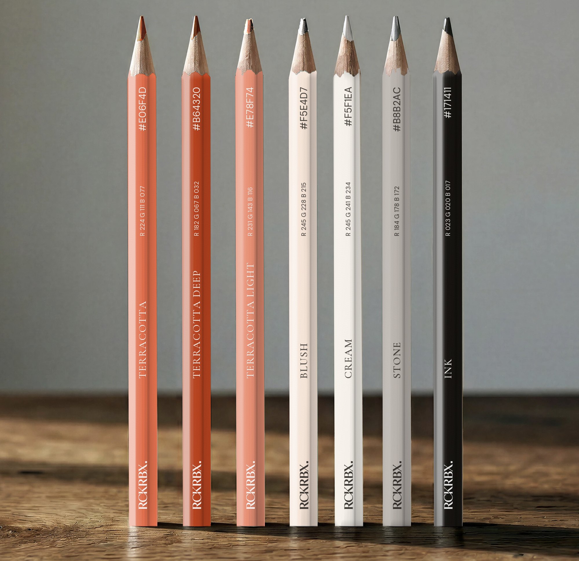 Seven RCKRBX pencils standing on a wooden table, each printed with a palette name and value: Terracotta, Terracotta Deep, Terracotta Light, Blush, Cream, Stone, Ink