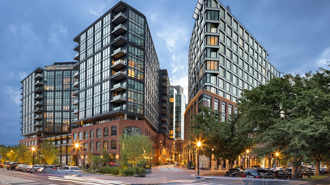 Photograph of The Stacks at dusk: glass towers over brick-warehouse bases, lit from the street