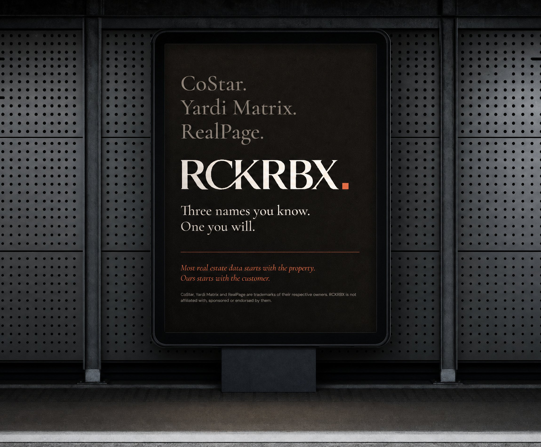 A backlit poster in a dark perforated-steel transit wall: CoStar, Yardi Matrix, RealPage, then the RCKRBX wordmark and Three names you know. One you will.