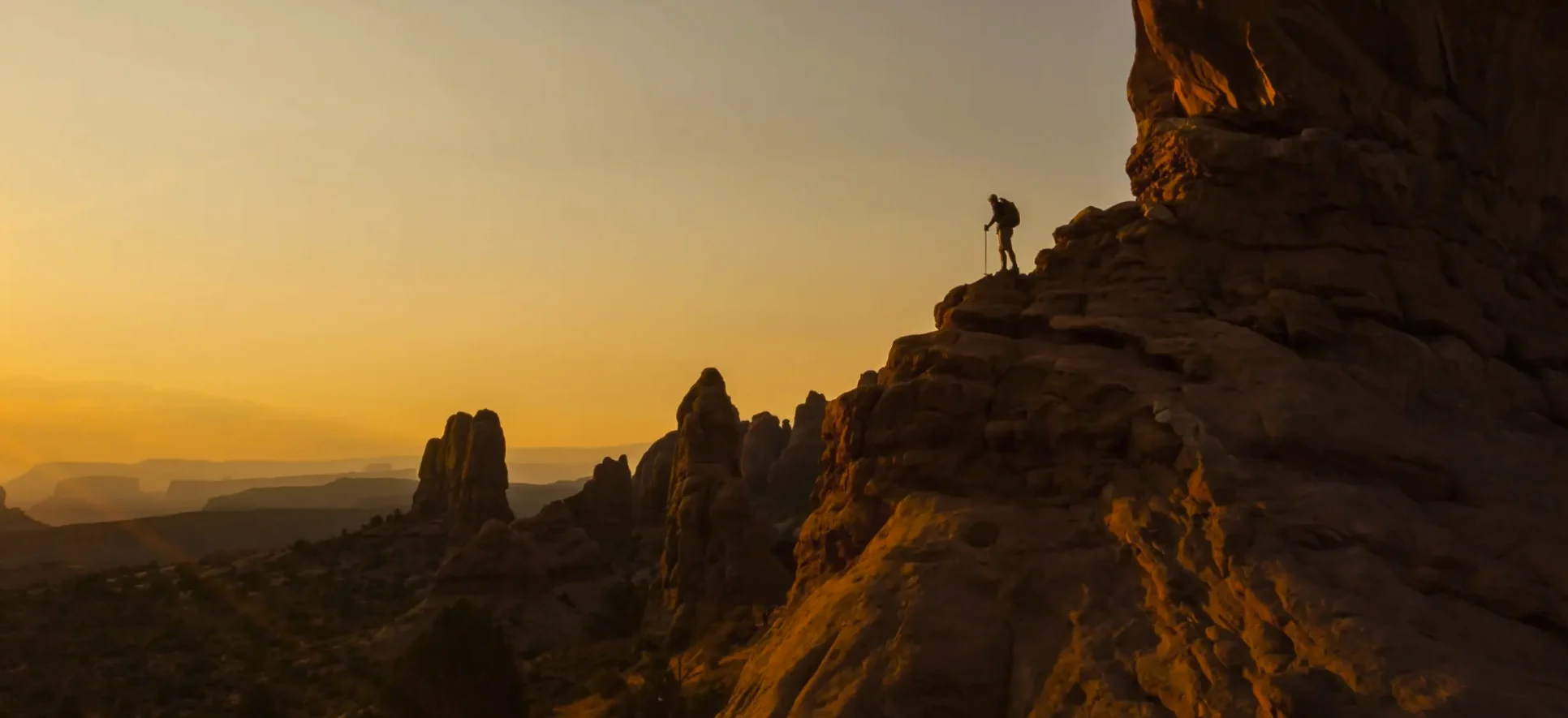 A hiker on a sandstone ridge at sunset above the Moab valley